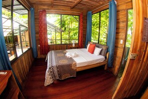 A wooden room with a bed, a window, and a view of greenery. - Terrazas del Golfo  (Puerto Jiménez)