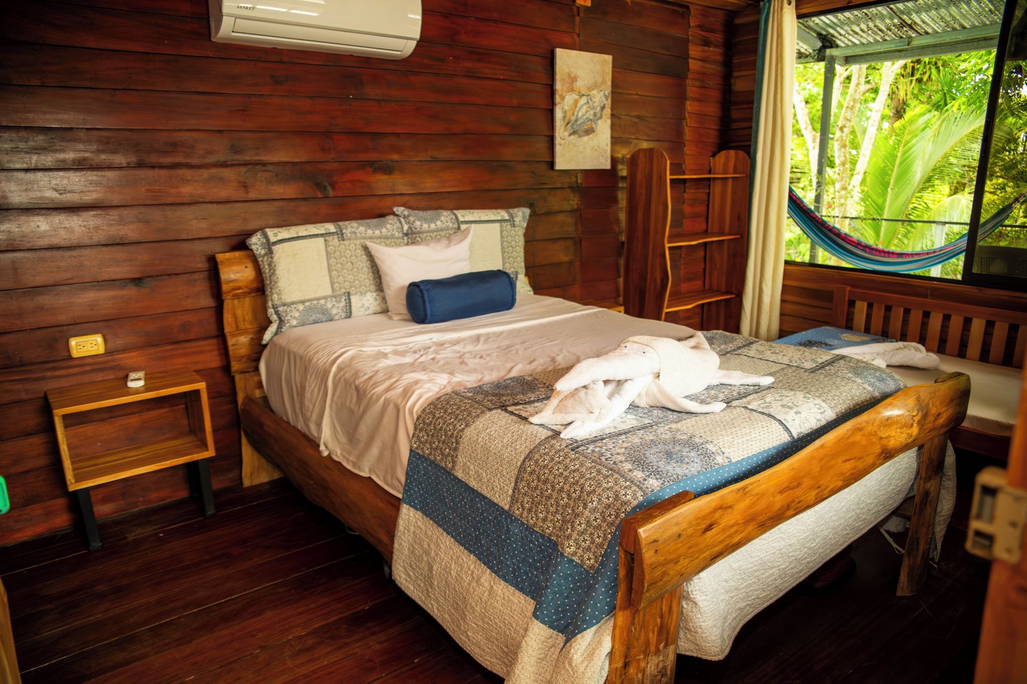Une pièce de cabane en bois comprenant un lit, un hamac et une fenêtre donnant sur un paysage verdoyant.