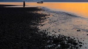 A beach at sunset with a person walking, a boat in the water, and mountains in the background. - Terrazas del Golfo (Puerto Jiménez)