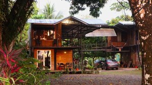 A two-story wooden house with a covered porch, surrounded by lush vegetation. - Terrazas del Golfo (Puerto Jiménez)
