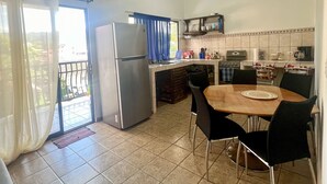 A kitchen with a refrigerator, stove, and dining table with chairs. - Apartamento Centro de Jaco, 100 Metros Playa, Comercios (Jacó)