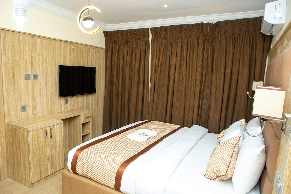 Habitación de hotel con cama, televisión de pantalla plana, armario de madera y cortina.