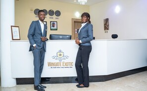 A reception desk with a logo for Wingate Exotic hotel, featuring a clock, framed photos, and a computer. - Wingate Exotic (Ilorin)