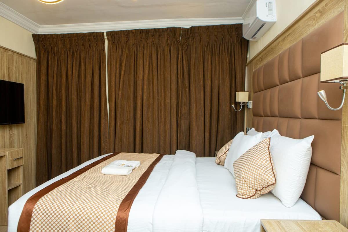 Habitación de hotel con una cama grande, un armario de madera, un televisor de pantalla plana y un equipo de aire acondicionado instalado en la pared.