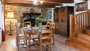 Un comedor con chimenea de piedra, sillas de madera, una mesa redonda y una escalera.