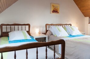 Twee houten bedden met wit beddengoed en groene accenten, een nachtkastje met een lamp, en een schilderij aan de muur.