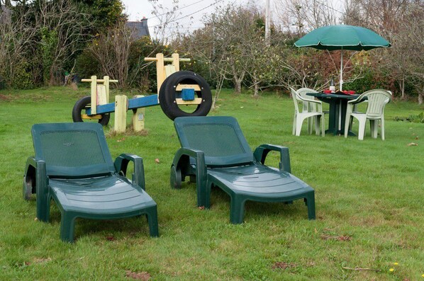 Deux chaises de jardin vertes et une petite table avec un parasol vert, le tout installé dans un espace extérieur verdoyant.