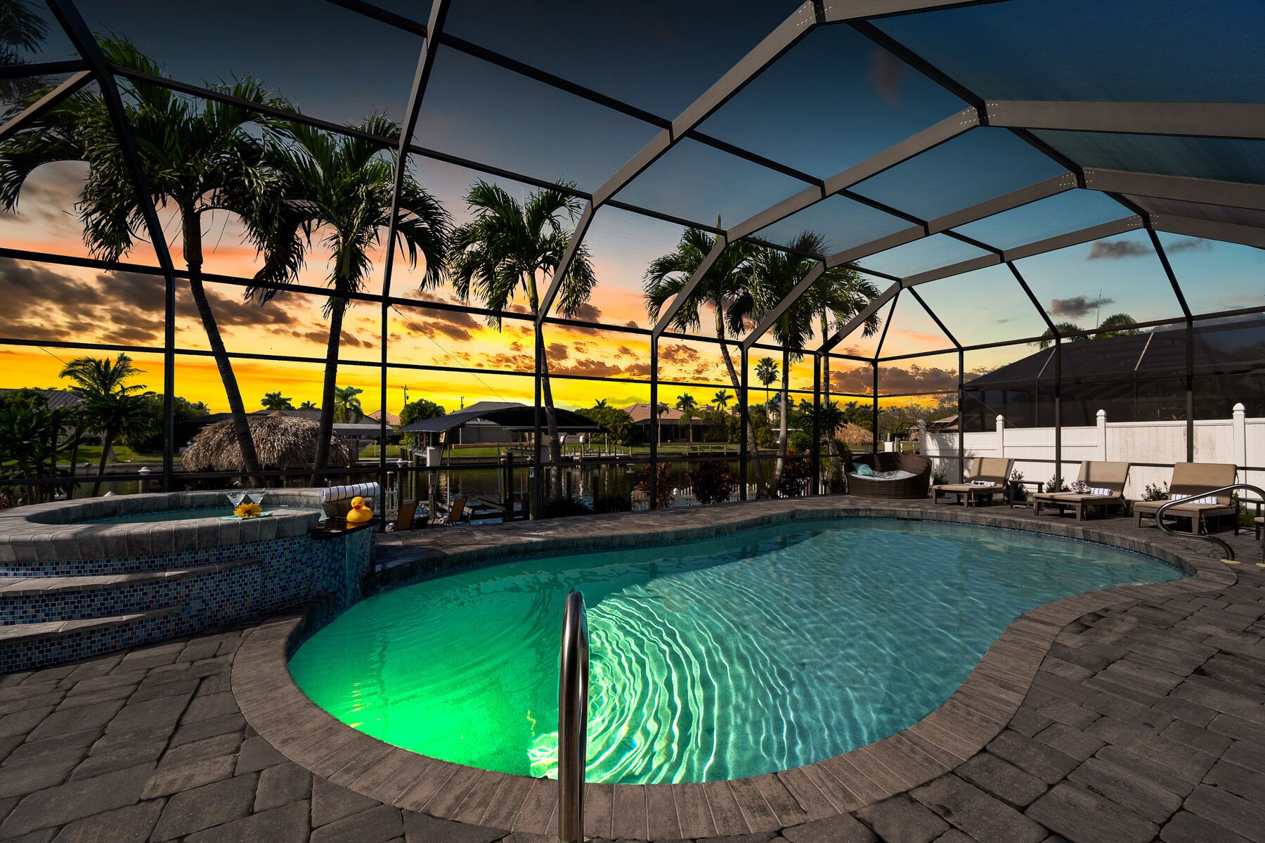 Une piscine intérieure offrant une vue dégagée sur le coucher de soleil et les palmiers à l’extérieur.