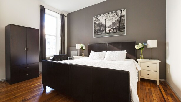 Een slaapkamer met een groot bed, een kledingkast, een nachtkastje met een lamp en een aan de muur hangend schilderij.