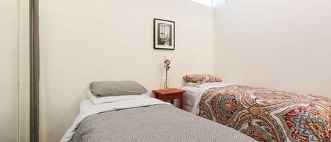 A bedroom with two beds, a small wooden nightstand, a framed picture on the wall, and a window providing natural light.