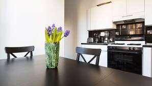 Een moderne keuken met witte kastjes, een zwarte kookplaat en een vaas met paarse bloemen op de eettafel.