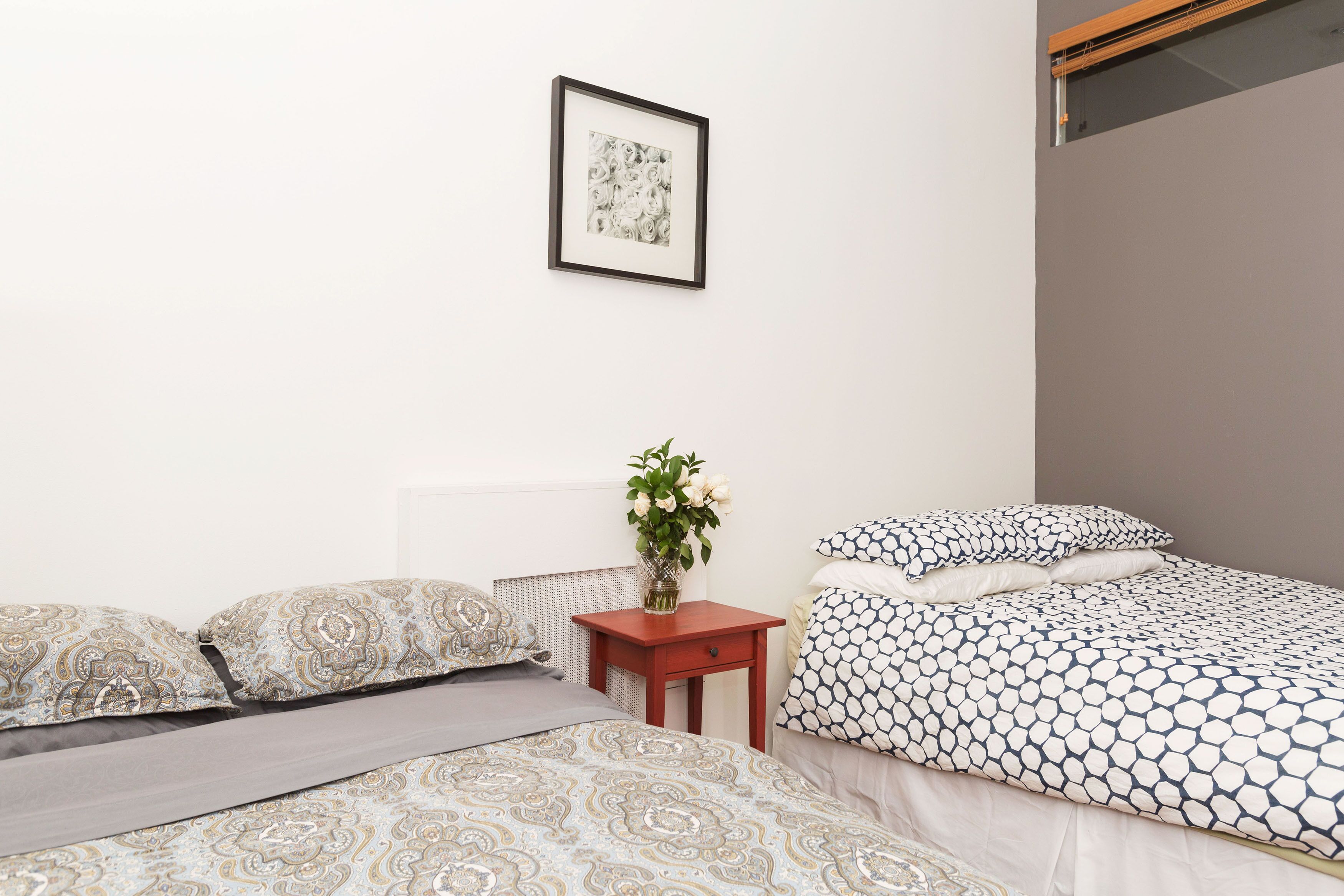 Une chambre avec deux lits, une table de chevet ornée d’un vase de fleurs et un tableau encadré accroché au mur.