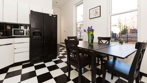 Een moderne keuken met een zwart-wit geruite vloer, een zwarte koelkast, witte kasten, een magnetron en een eettafel met stoelen.
