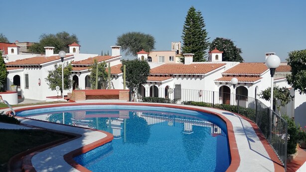A swimming pool with a red and white border, surrounded by a white building with red-tiled roofs and a clear blue sky. - Villas Tequisquiapan  (Tequisquiapan)