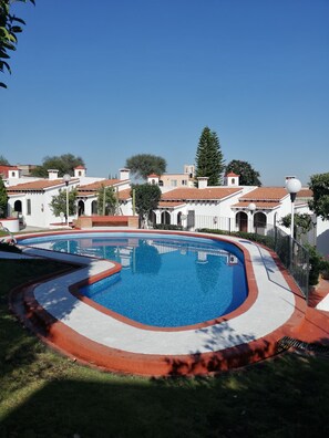A swimming pool with a red and white border, surrounded by a white building with red-tiled roofs and a clear blue sky. - Villas Tequisquiapan  (Tequisquiapan)