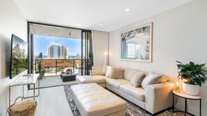 Uma sala de estar moderna com um sofá grande, uma mesa de centro e vista para um horizonte urbano através de janelas do chão ao teto.