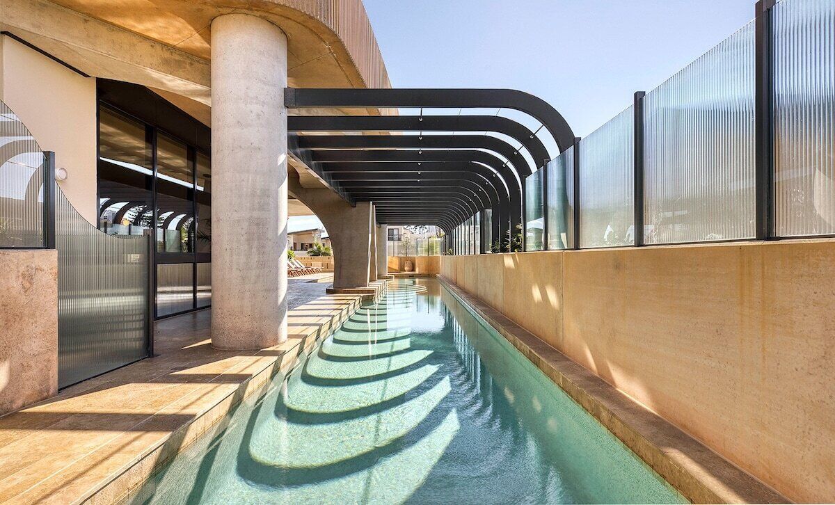 Un bâtiment moderne doté d’un long bassin étroit qui le traverse de part en part, flanqué de grandes colonnes en béton et de murs en verre.