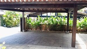 A covered outdoor area with a tiled floor, surrounded by plants and a brick wall.