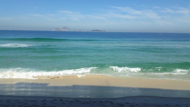 A beach with clear blue water, a sandy shore, and distant islands.