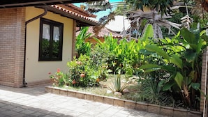 A brick building with a tiled patio and a garden with various plants and flowers.