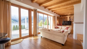 Un salon spacieux avec un grand canapé, un plancher en bois et une vue sur un lac et des montagnes, grâce à de grandes fenêtres.