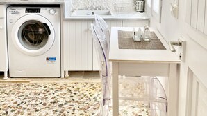 A compact kitchen with a washing machine, microwave, and a small dining area. - CABARNUS HOUSE in the HEART of Paroikia, Paros! (Paros)