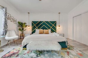 Quarto com cama, cadeira, planta e obras de arte na parede.