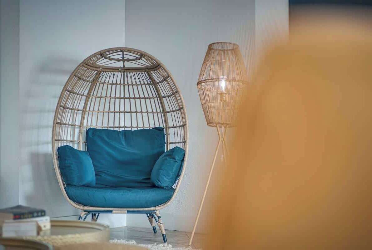 Et værelse med en fletstol, en høj gulvlampe og en bogreol.