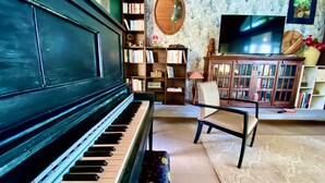 Una habitación con un piano, una estantería, una silla y un televisor.