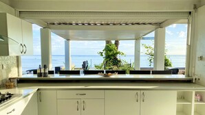 Una cocina con armarios blancos, una estufa a gas y vista al océano.