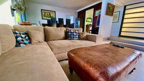 Una sala de estar con un sofá color beige, un reposapiés de cuero marrón y un televisor sobre un mueble.