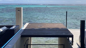 Terraza de madera con vistas a aguas turquesas y una persona practicando kitesurf a lo lejos.