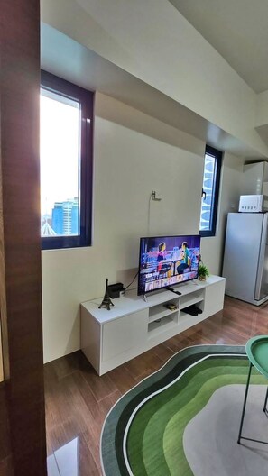Un salon moderne avec un téléviseur à écran plat posé sur un meuble blanc, un fauteuil vert et un tapis à motifs.