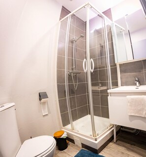 Baño con ducha de vidrio, inodoro, lavamanos y espejo.