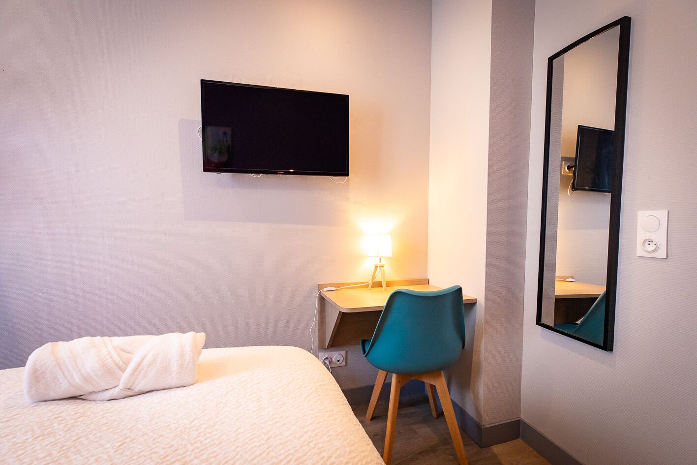 A hotel room with a bed, a desk, a chair, a television, and a mirror.