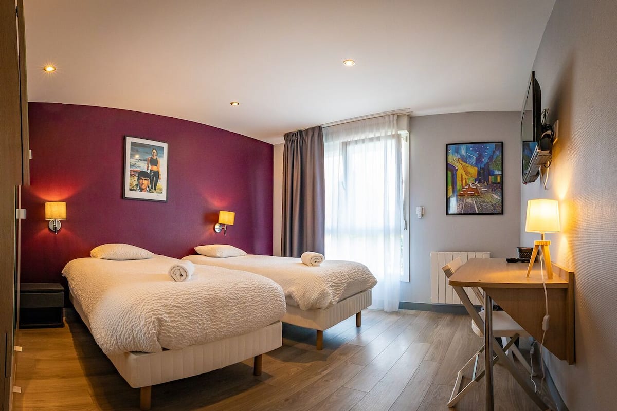 A hotel room with two beds, a desk, and a window with curtains.