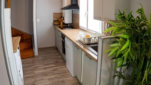 A compact kitchen with wooden flooring, a built-in stove, and a large green plant. - Résidence Hera Paris Orly Aéroport (Villeneuve-le-Roi)