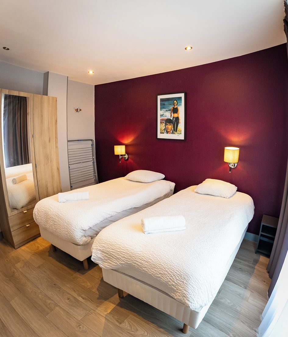 A hotel room with two beds, a wooden wardrobe, a mirror, and a painting on the wall.