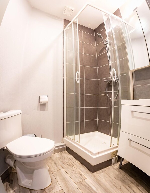 A modern bathroom with a glass-enclosed shower, a toilet, and a vanity with drawers.