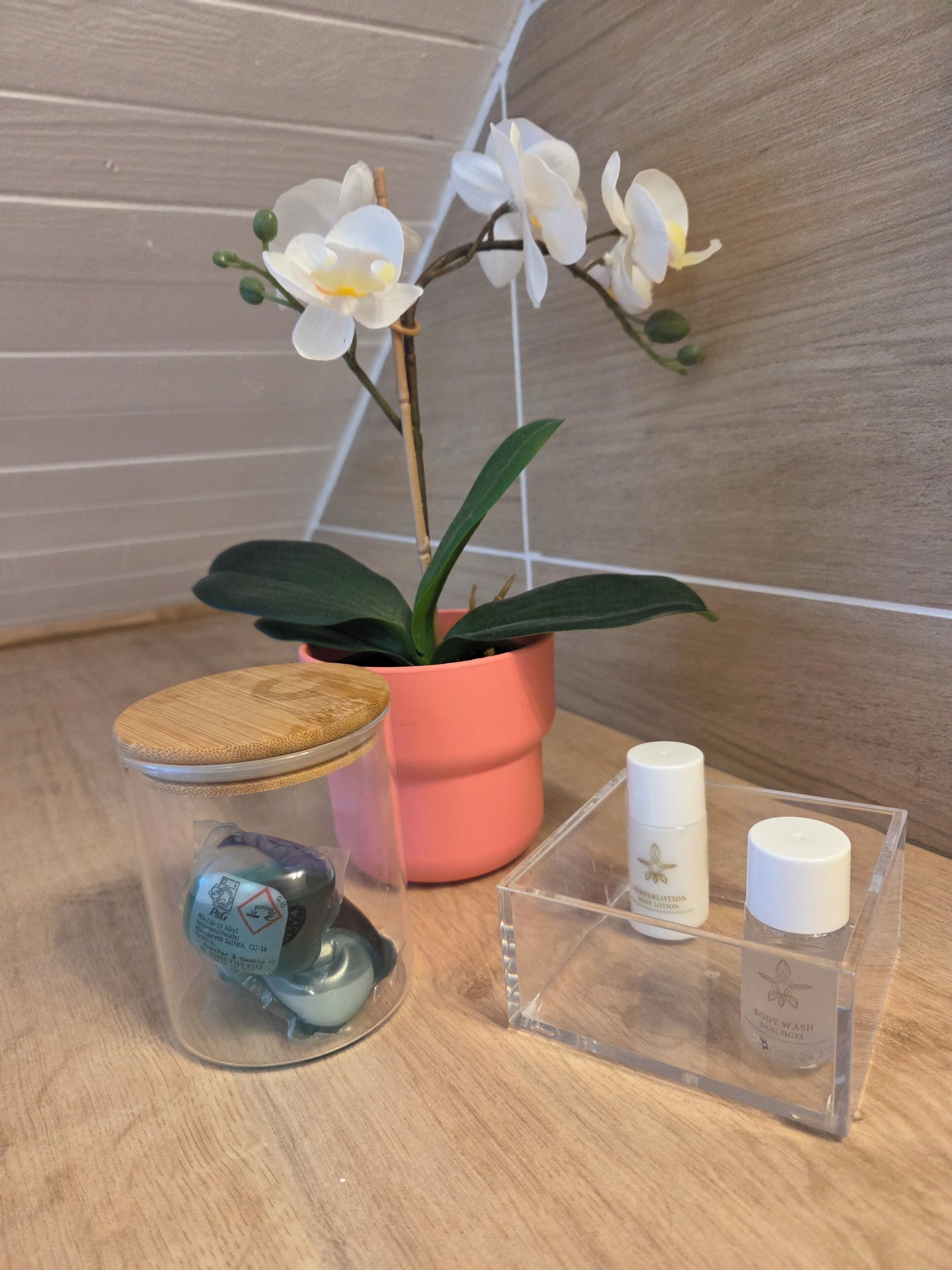 A potted orchid, a jar with a cork lid, and two bottles on a wooden surface.