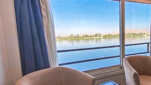 A room with two chairs and a small table, large windows with a view of a lake and distant mountains. - Nile Cruise Luxor&Aswon IncludingTours (Luxor)