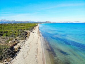 Un paisaje costero con una playa arenosa, agua azul cristalina y vegetación verde.