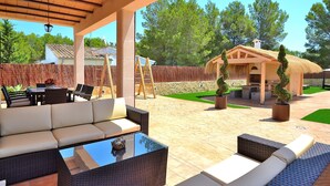 Un patio exterior con zona de estar cubierta, una estructura de techo de paja y un césped bien cuidado.