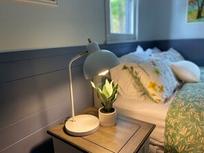 Een nachtkastje met een witte bureaulamp, een potplant en een bed met beddengoed met een patroon.
