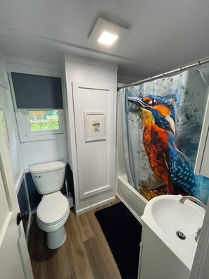 Een kleine badkamer met toilet, wastafel en douchegordijn met een vrolijk vogelmotief.