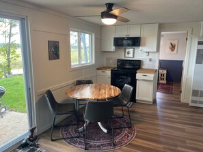 Een compacte keuken met een eethoek, met een ronde houten tafel, twee stoelen, een plafondventilator en een magnetron boven het fornuis.