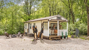 Une petite cabane dotée d’un porche, entourée d’arbres.