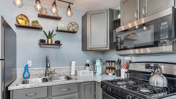 Une cuisine moderne dotée de plans de travail en granit, d’appareils électroménagers en acier inoxydable et d’étagères décoratives murales.