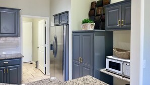 Une cuisine moderne avec des meubles de couleur gris foncé, un réfrigérateur en acier inoxydable, un four à micro-ondes et des plans de travail en granit.