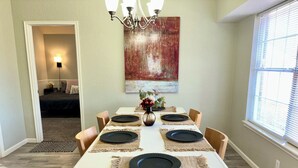 Un espace repas avec une table blanche, des assiettes noires et des chaises en bois.